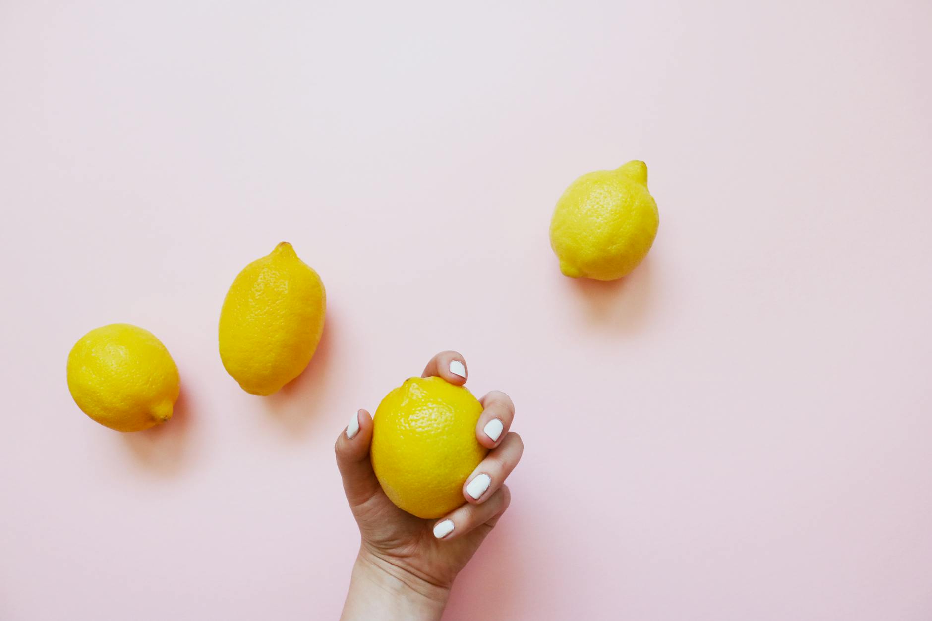 A hand holding a bright yellow lemon on a soft pink background, symbolizing natural pleasure and self-care.