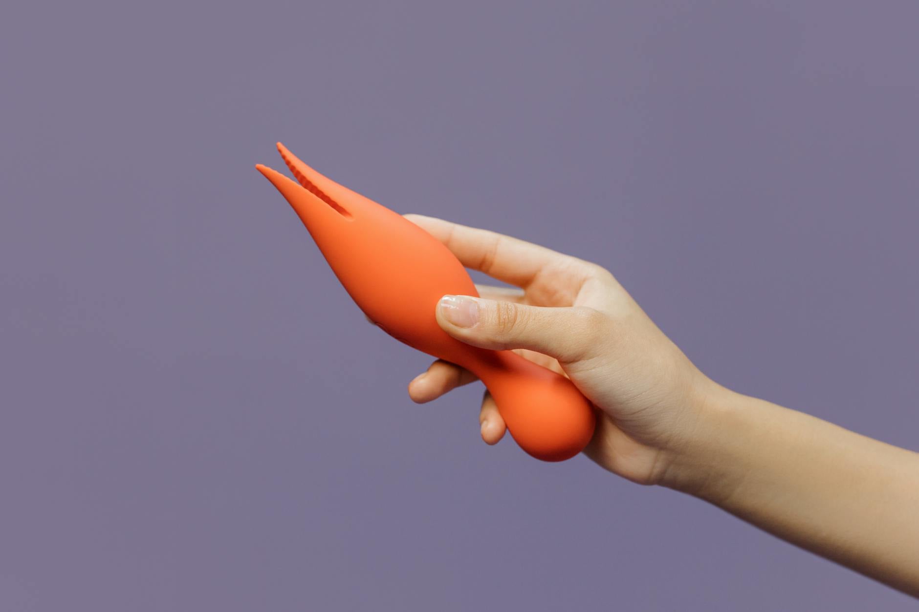 A hand holding a lemon-colored vibrator against a minimalist purple backdrop.