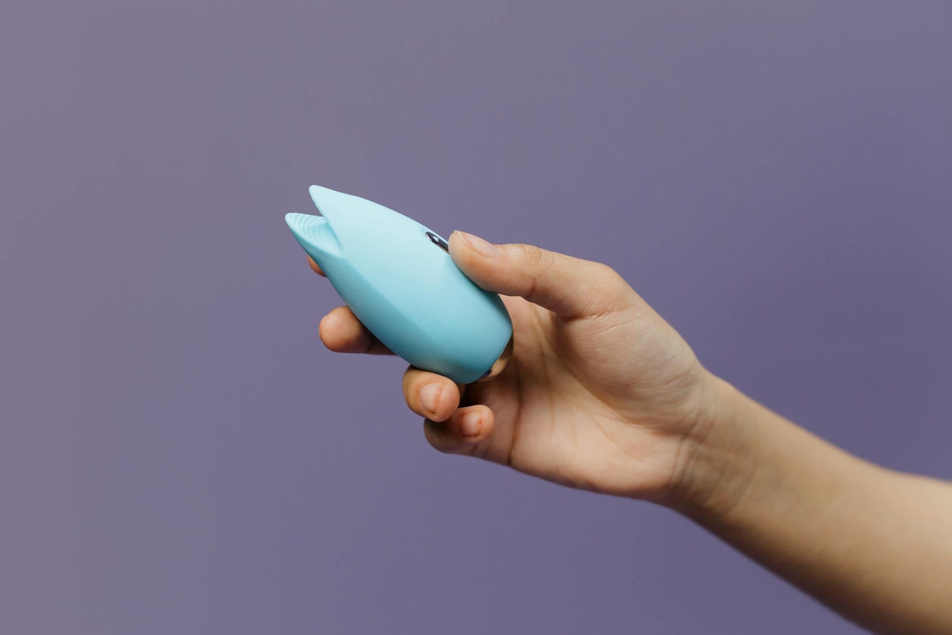 A hand holding a blue silicone vibrator against a purple background, showcasing pleasure and self-care