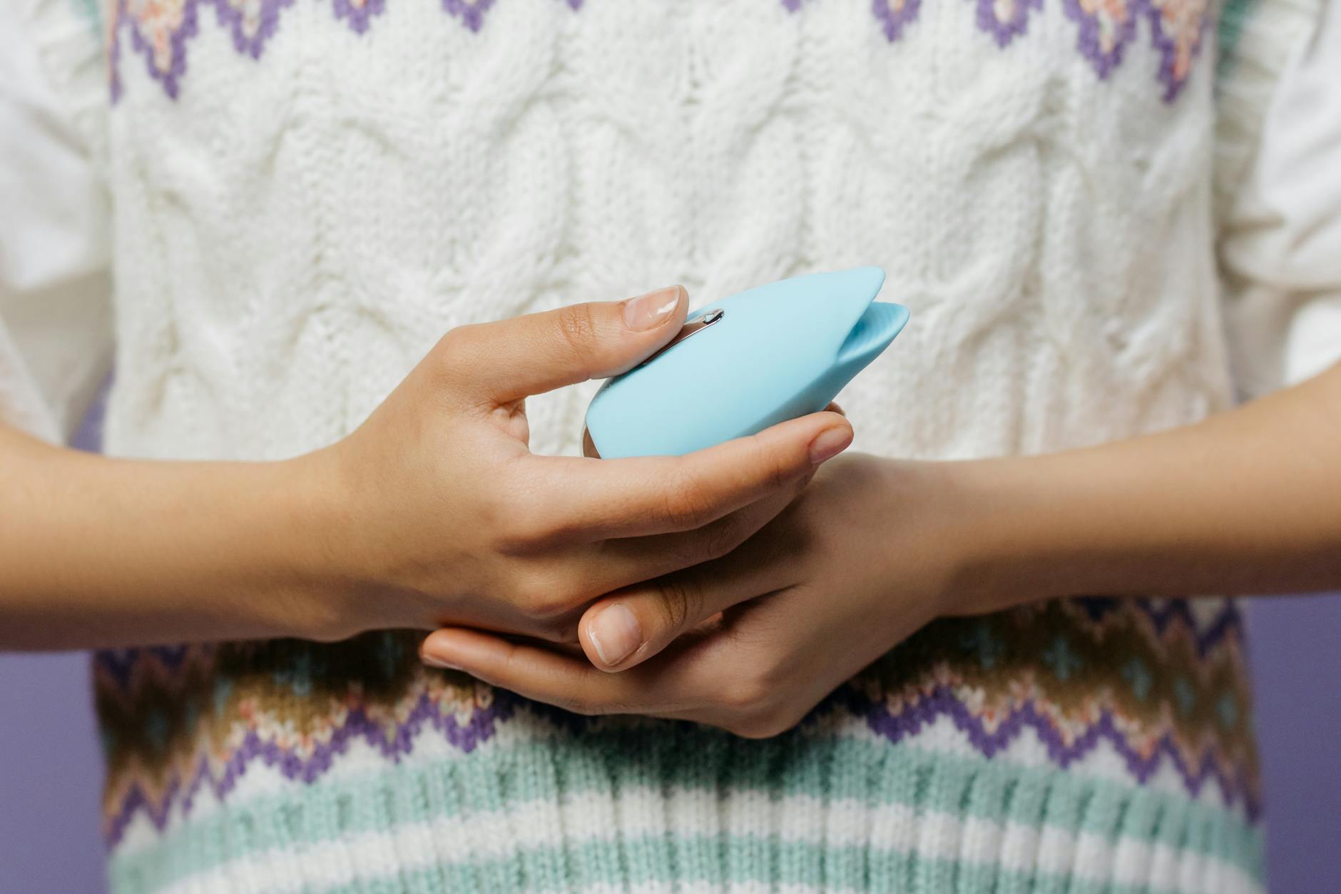 Close-up of hands holding a blue personal massager against a knitted sweater, showing grounding through touch.